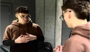 Молодий барбер в коричневому худі за роботою перед дзеркалом