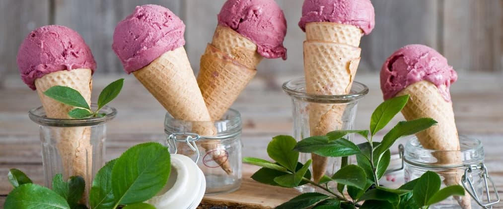 Violet ice cream cones sitting in glass jars and decorated with peppermint leaves.